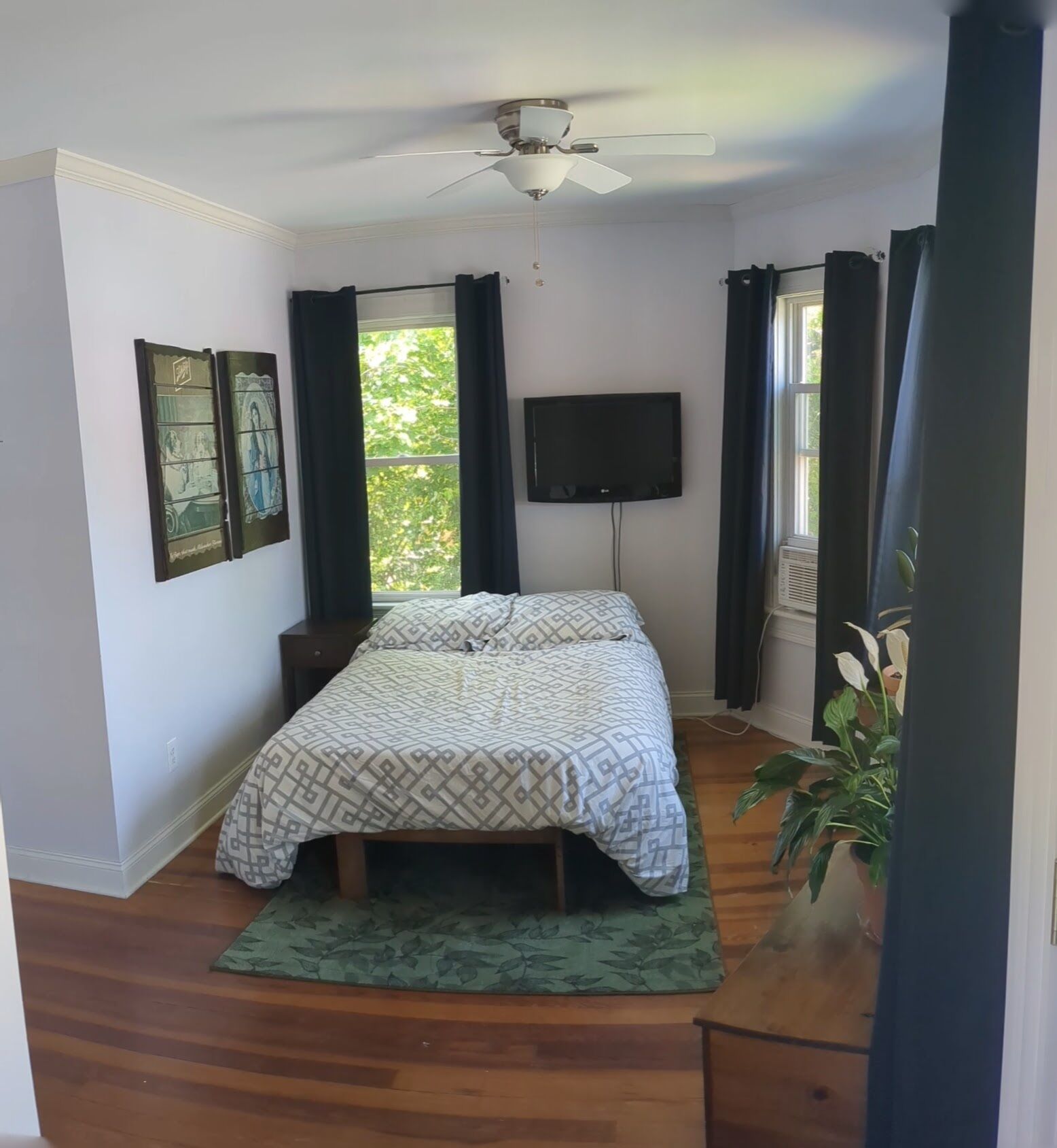 Una camera da letto con un letto, una ventola a soffitto, una TV e una finestra con tende.