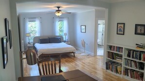 A bedroom with a bed, bedside table, and a fan. There is a wooden desk with a laptop and a chair. A bookshelf with books is visible in the background. - Spacious 5-bedroom House, Walking Distance to Williams (Williamstown)