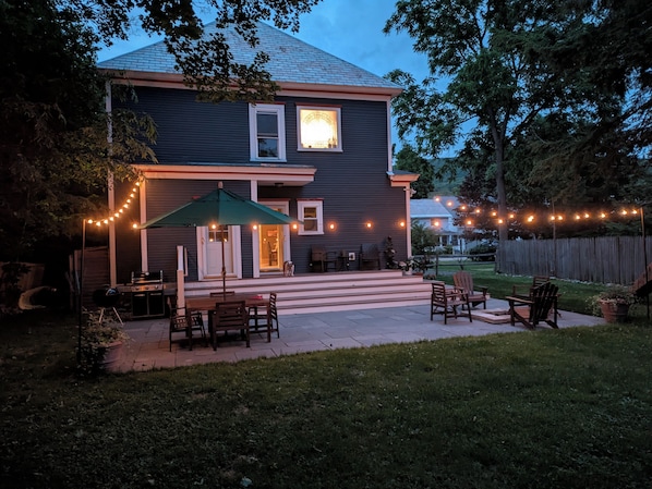 Una casa con patio, mobiliario exterior e iluminación de luces colgantes.