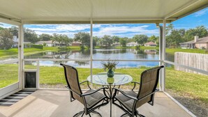 A covered patio with two chairs and a table, overlooking a calm lake and residential homes. - Water View Retreat | spacious 3br w/ lanai (Jacksonville)
