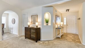 A spacious hallway with a dark wooden cabinet, a white door, and a small table with two lamps. - Water View Retreat | spacious 3br w/ lanai (Jacksonville)