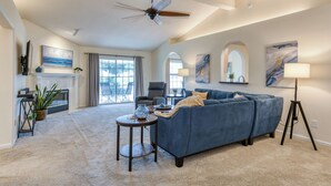 A spacious living room with a large blue sofa, a fireplace, a ceiling fan, and a view through large glass doors. - Water View Retreat | spacious 3br w/ lanai (Jacksonville)