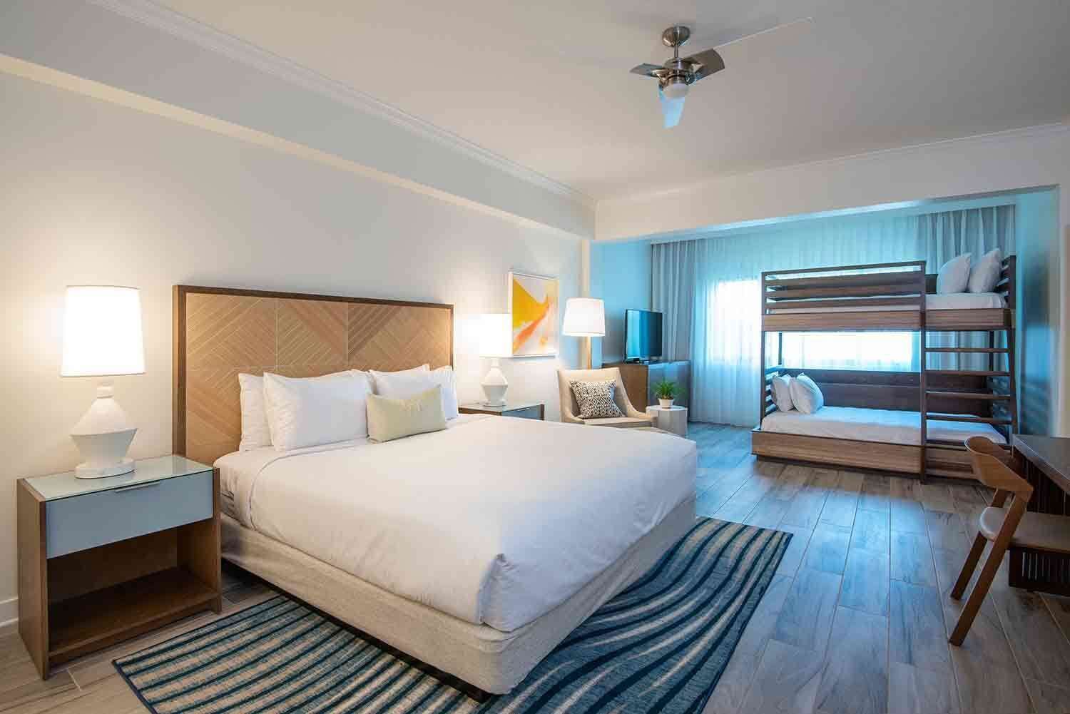 Ein Hotelzimmer mit einem großen Bett, einem Schreibtisch, einem Sessel, einem Fernseher und einem Balkon mit Blick.