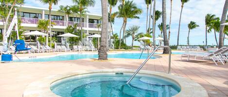 A pool area with lounge chairs, palm trees, and a hot tub.