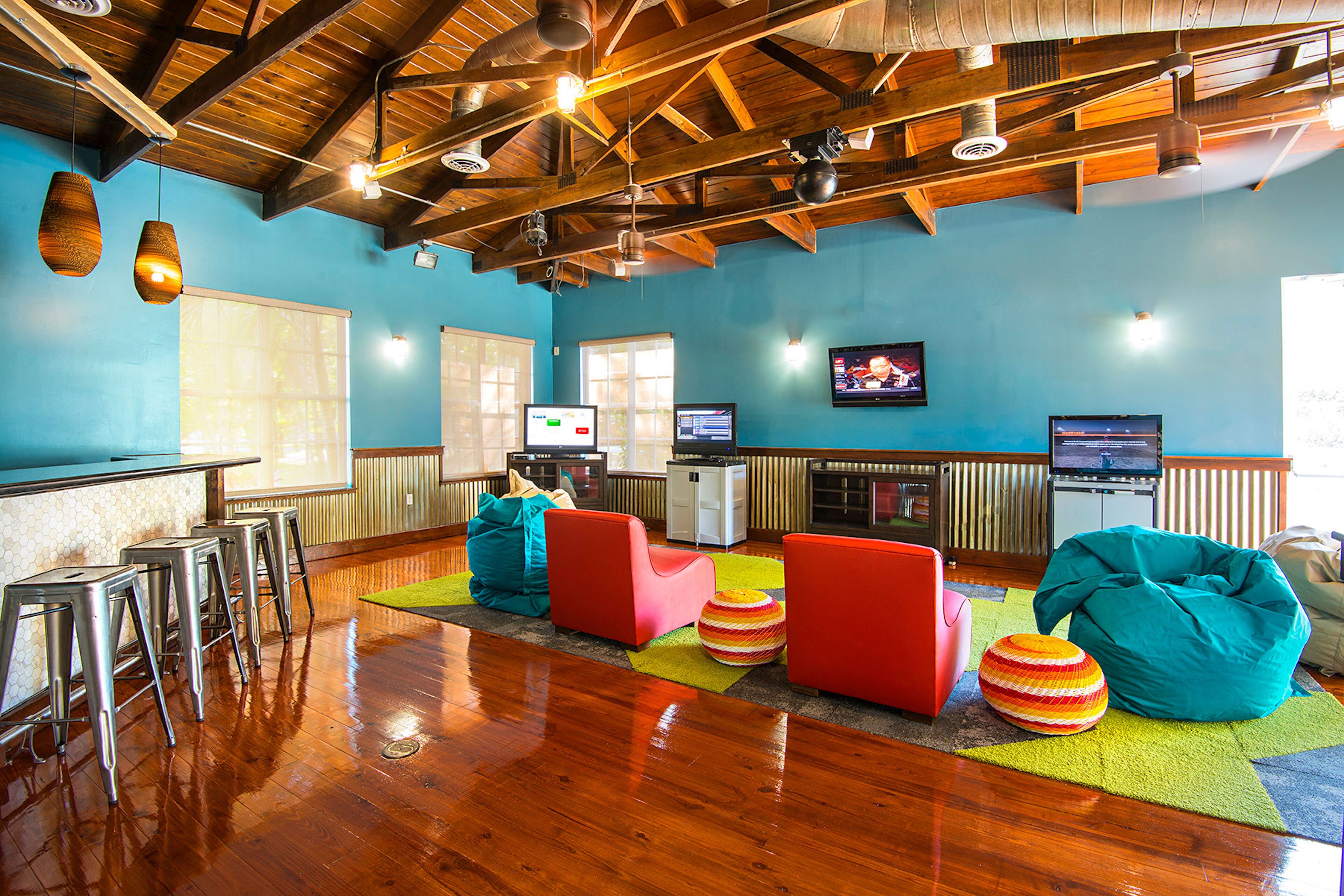 A spacious room with wooden beams, a bar area with stools, colorful seating, and a television.