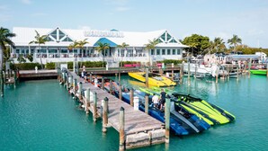 Un hôtel situé au bord de l’eau, doté d’une jetée qui s’avance sur l’eau, où sont amarrés différents types de bateaux, et d’un grand bâtiment dont le toit se distingue particulièrement.
