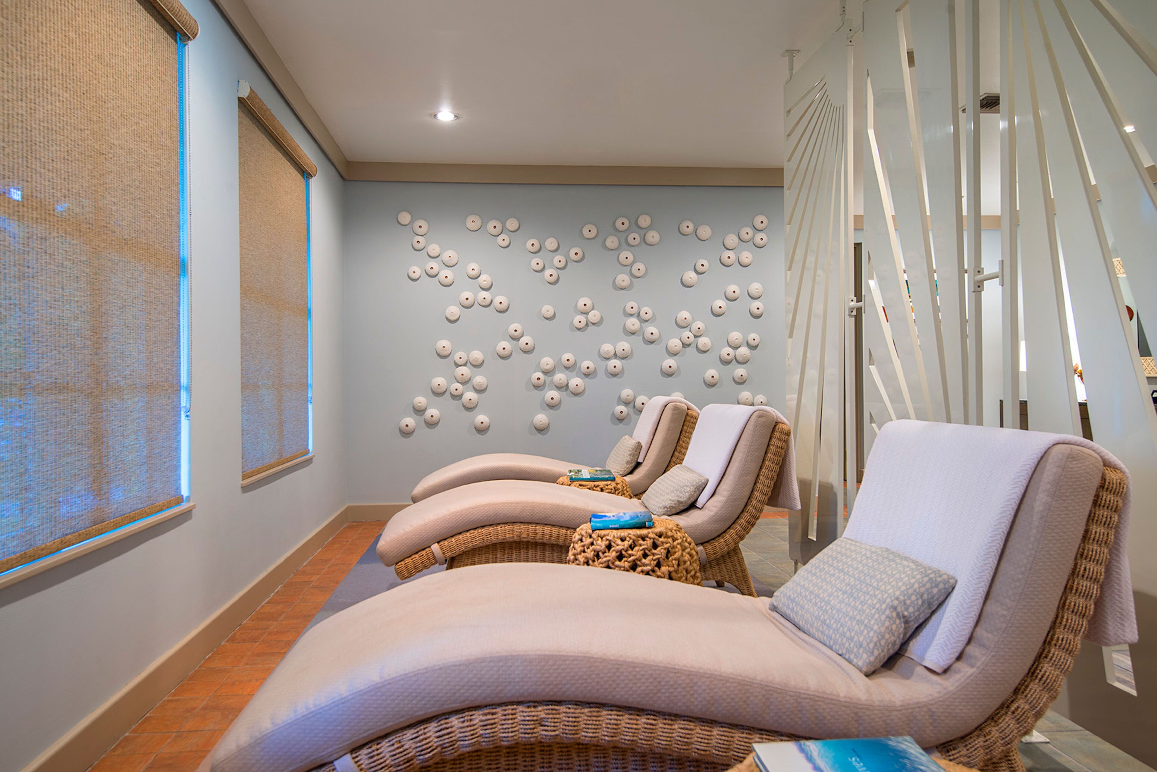 A spa room with three reclining chairs, a wall with decorative spherical objects, and a staircase with white railings.