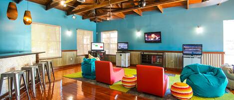 A spacious room with wooden beams, a bar area with stools, colorful seating, and a television.