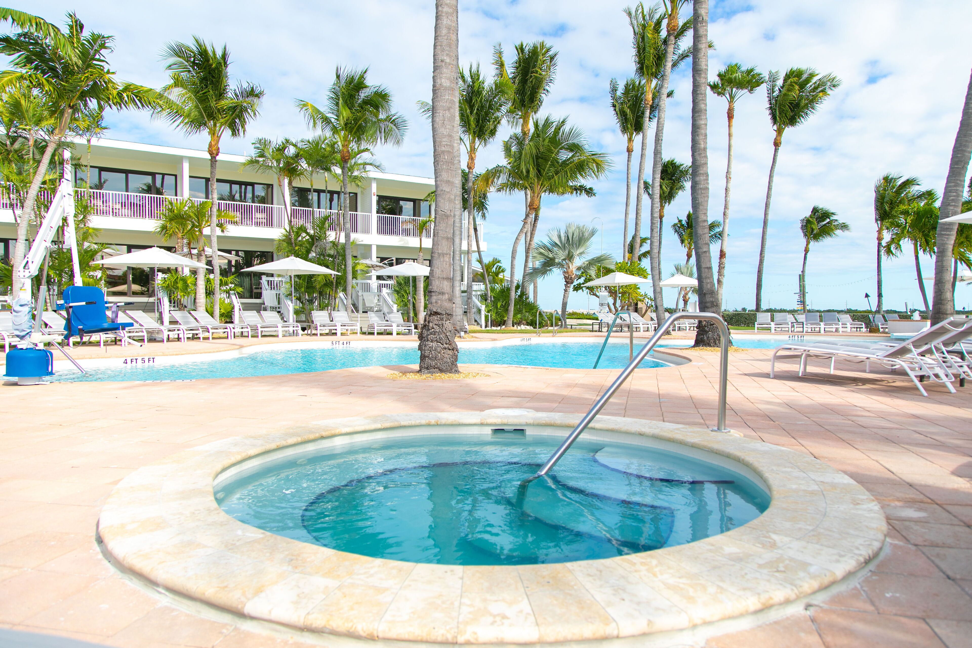 Un espace piscine dot é de chaises longues, de palmiers et d’un jacuzzi.