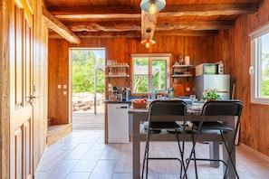 A wooden interior with a kitchen area, dining table, chairs, and a view through a door to an outdoor patio. - Le Chalet Des Oliviers: private pool, Wi-Fi, and air conditioning in Roquefort-la-Bédoule (Roquefort-la-Bédoule)