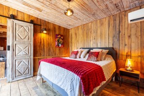 A wooden-paneled room with a bed, a wall-mounted air conditioner, and a door with a geometric design. - Le Chalet Des Oliviers: private pool, Wi-Fi, and air conditioning in Roquefort-la-Bédoule (Roquefort-la-Bédoule)