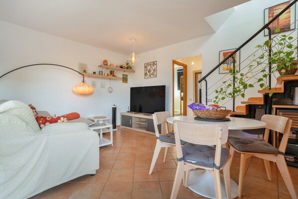 Una sala de estar con sofá, televisor, mesa de comedor, sillas y una escalera.