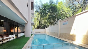 Una piscina con un borde de baldosas, rodeada por un muro bajo y una banca.