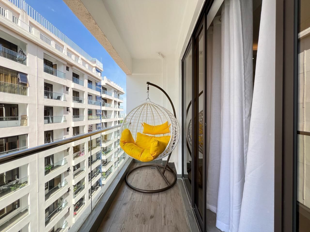 A balcony with a hanging chair, a view of adjacent buildings, and a glass door.