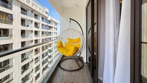 Un balcón con una silla colgante, vista de edificios cercanos y una puerta de cristal.