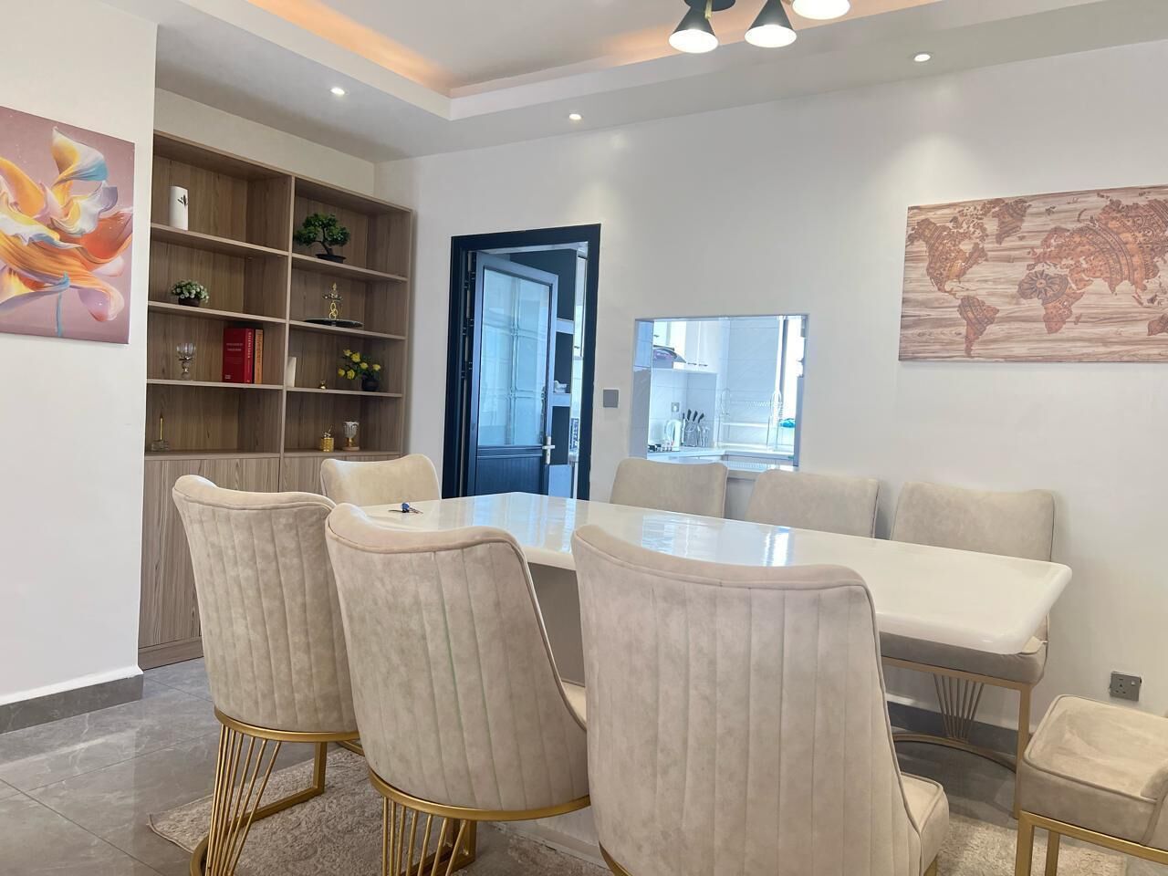 A dining area with a white table and matching chairs, a wooden bookshelf, and a world map on the wall.
