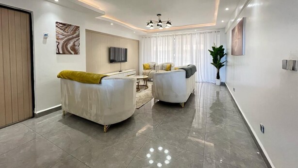 Una sala de estar moderna con dos sofás blancos, una mesa de centro y un televisor en la pared.