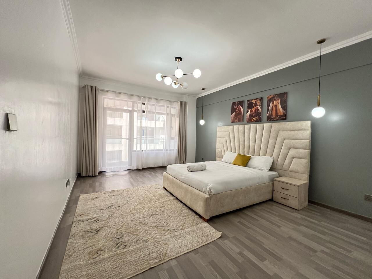 A modern bedroom with a large bed, a bedside table, a nightstand, a floor lamp, and a window with curtains.