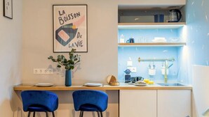 A modern kitchen with a blue countertop, two blue chairs, a framed artwork, and a blue vase with green leaves. - Black & White Studio downtown- M2 metro 4-6 tram (Budapest)