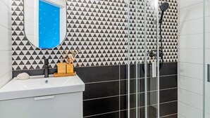 A bathroom with a geometric patterned wall, a mirror, a sink, and a shower area. - Black & White Studio downtown- M2 metro 4-6 tram (Budapest)