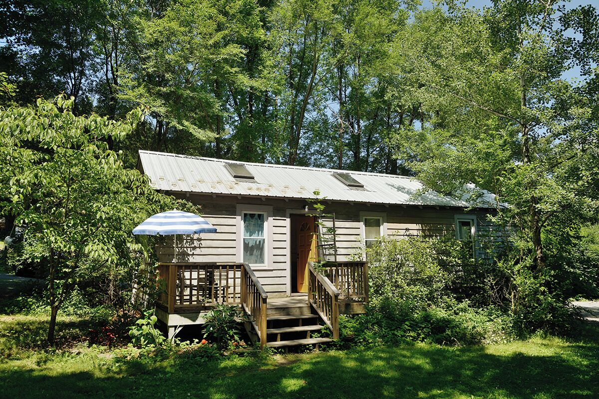 A rustic cabin with a wooden deck, a covered porch, and a staircase leading to the entrance.
