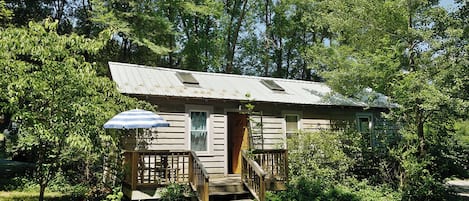 A rustic cabin with a wooden deck, a covered porch, and a staircase leading to the entrance.
