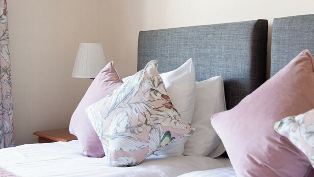 A neatly made bed with floral-patterned pillows, a grey headboard, and a bedside lamp.