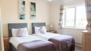 A double room with two beds, each with a headboard, a bedside table with a lamp, and a window with curtains.