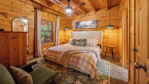 Ein gemütliches Schlafzimmer in einer Holzhütte, mit einem Bett, einem kleinen Tisch und einem Deckenventilator.