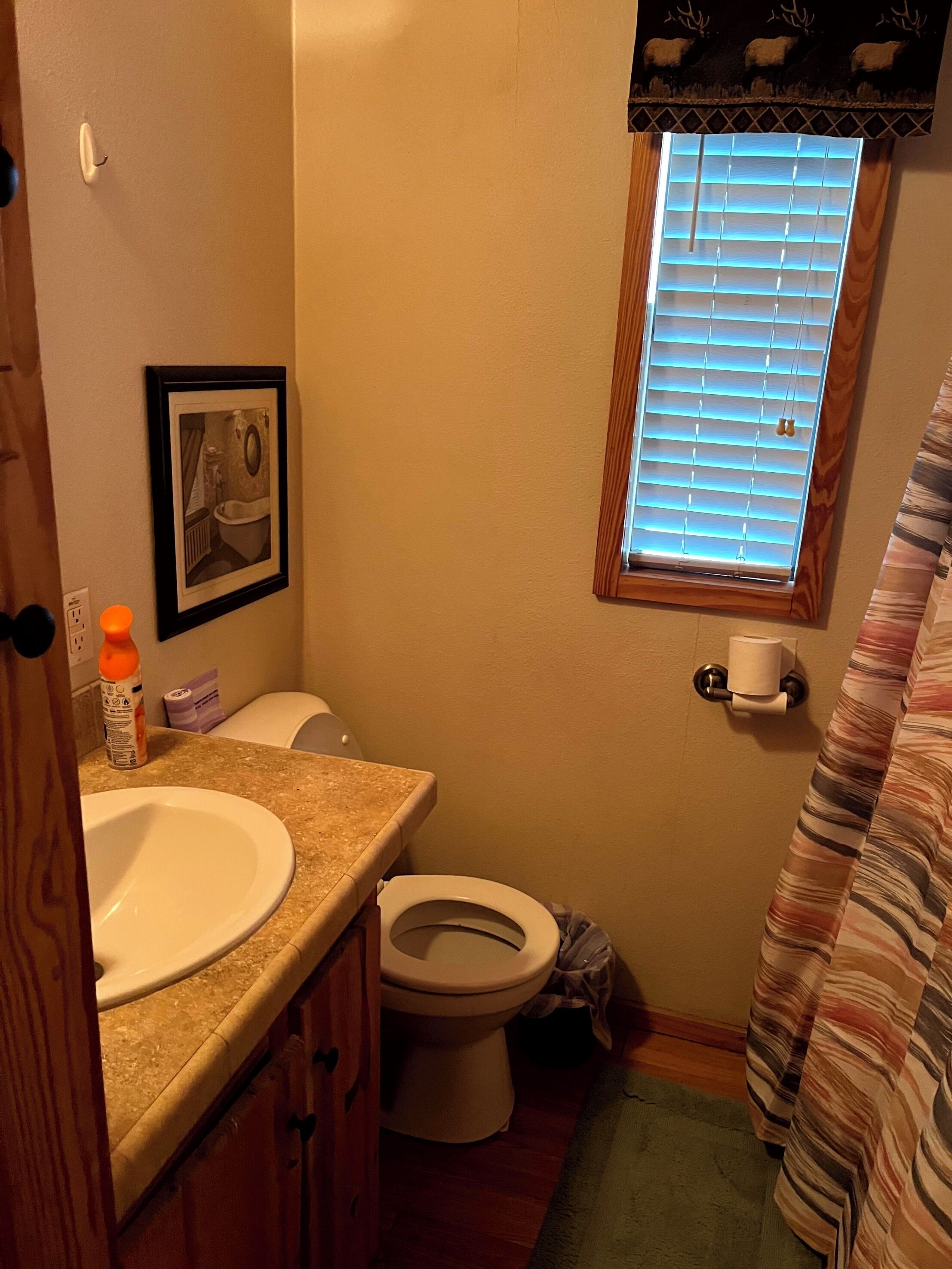 Ein kleines Badezimmer mit Toilette, Waschbecken und Fenster mit Jalousien.