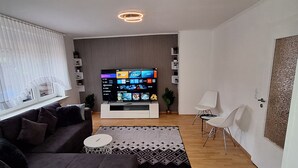 Una sala moderna con un sofá de color oscuro, una mesita redonda y un televisor de pantalla plana, además de una alfombra estampada.