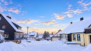 Eine Wohnstraße mit schneebedeckten Häusern, blauem Himmel und einer Straßenlaterne.