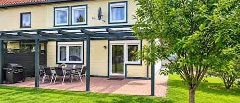Une maison avec un patio couvert, un barbecue et un arbre dans le jardin.