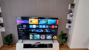 Un televisor de pantalla plana montado sobre un soporte blanco, con una pared a rayas verticales de fondo.