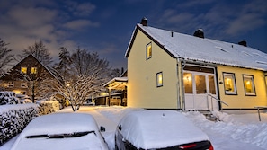 A snow-covered residential area with houses, a car, and a driveway.
