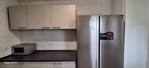 Eine Küche mit einem Edelstahl-Kühlschrank, einer Mikrowelle und hellen Schränken.