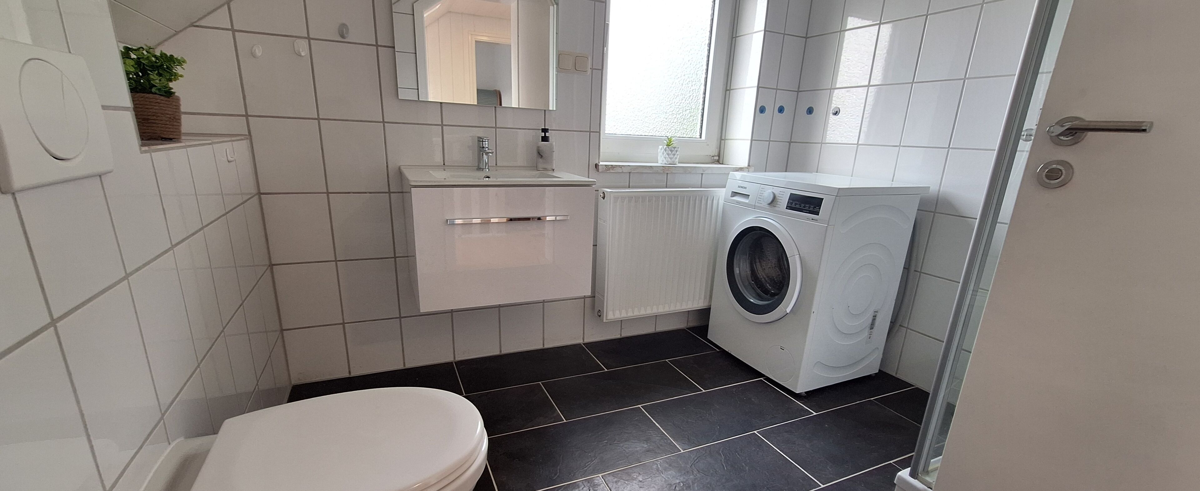 Ein kleines Badezimmer mit Toilette, Waschbecken, Spiegel, Waschmaschine und Heizkörper.