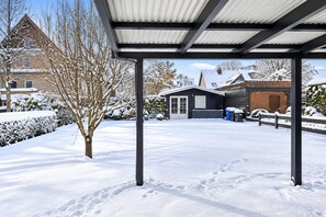A snow-covered outdoor area with a metal roof structure, a brick building, and a tree.