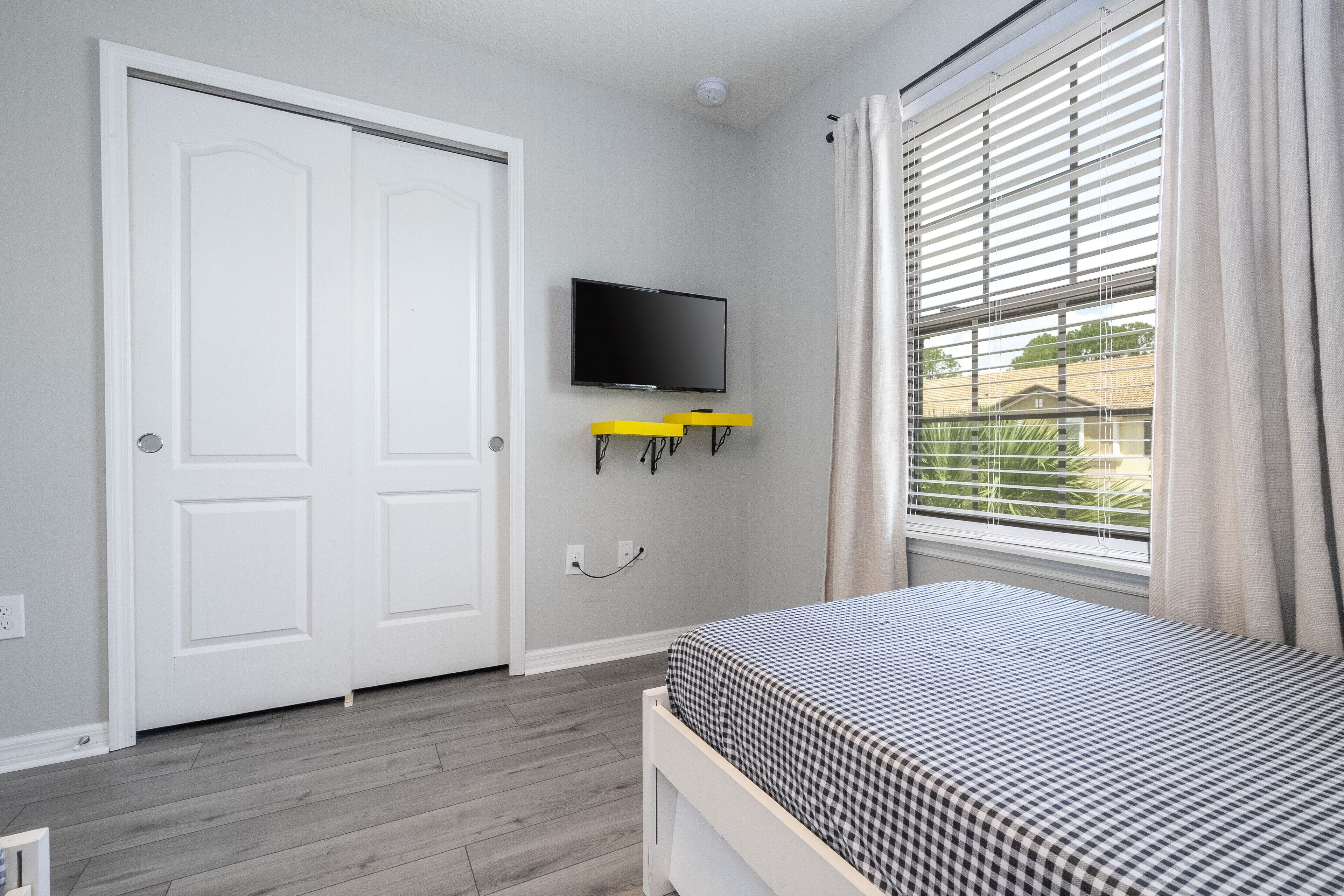 Een slaapkamer met een bed, een aan de muur bevestigde televisie, een deur en een raam met zonwering.