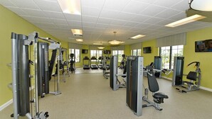 Une salle de sport équipée de divers appareils d’exercice, dotée de grandes fenêtres et d’un plafond recouvert de carreaux.