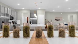 A modern kitchen with stainless steel appliances, a wooden dining table with glass vases, and a neutral color palette.
