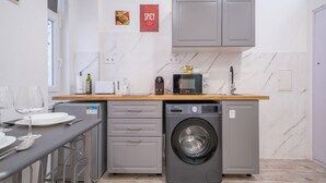 Una cocina funcional con lavadora, microondas y lavamanos. Hay armarios sobre la encimera y una ventana pequeña a la izquierda.