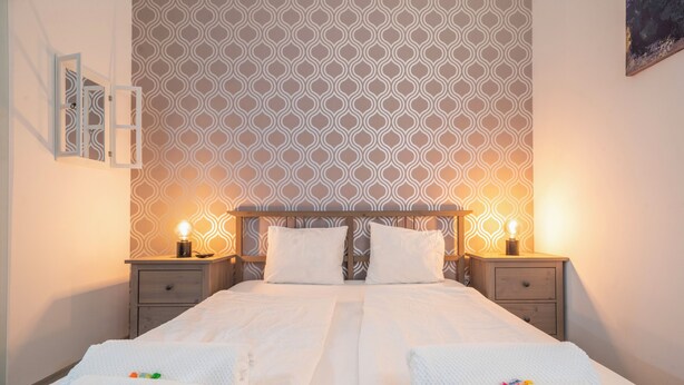 Una cama doble con cabecera estampada, dos mesitas de noche con lámparas, y una pared con diseño geométrico.