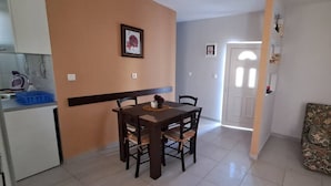 A dining area with a table and chairs, a sofa, and a kitchen area with a kettle and a blue container. - Apartments Janda Bijela (Bijela)