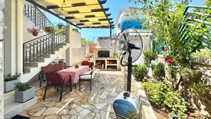 A patio with stone flooring, a table with chairs, a fan, and a barbecue area. - Apartments Janda Bijela (Bijela)
