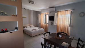 A bedroom with a bed, a dining table with chairs, a TV, and a clock on the wall. - Apartments Janda Bijela (Bijela)