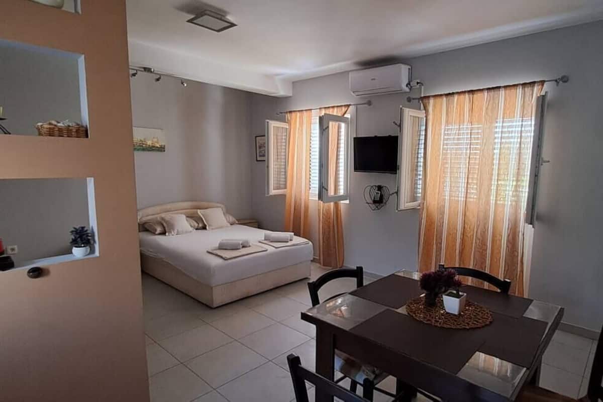 A bedroom with a bed, a dining table with chairs, a TV, and a clock on the wall.