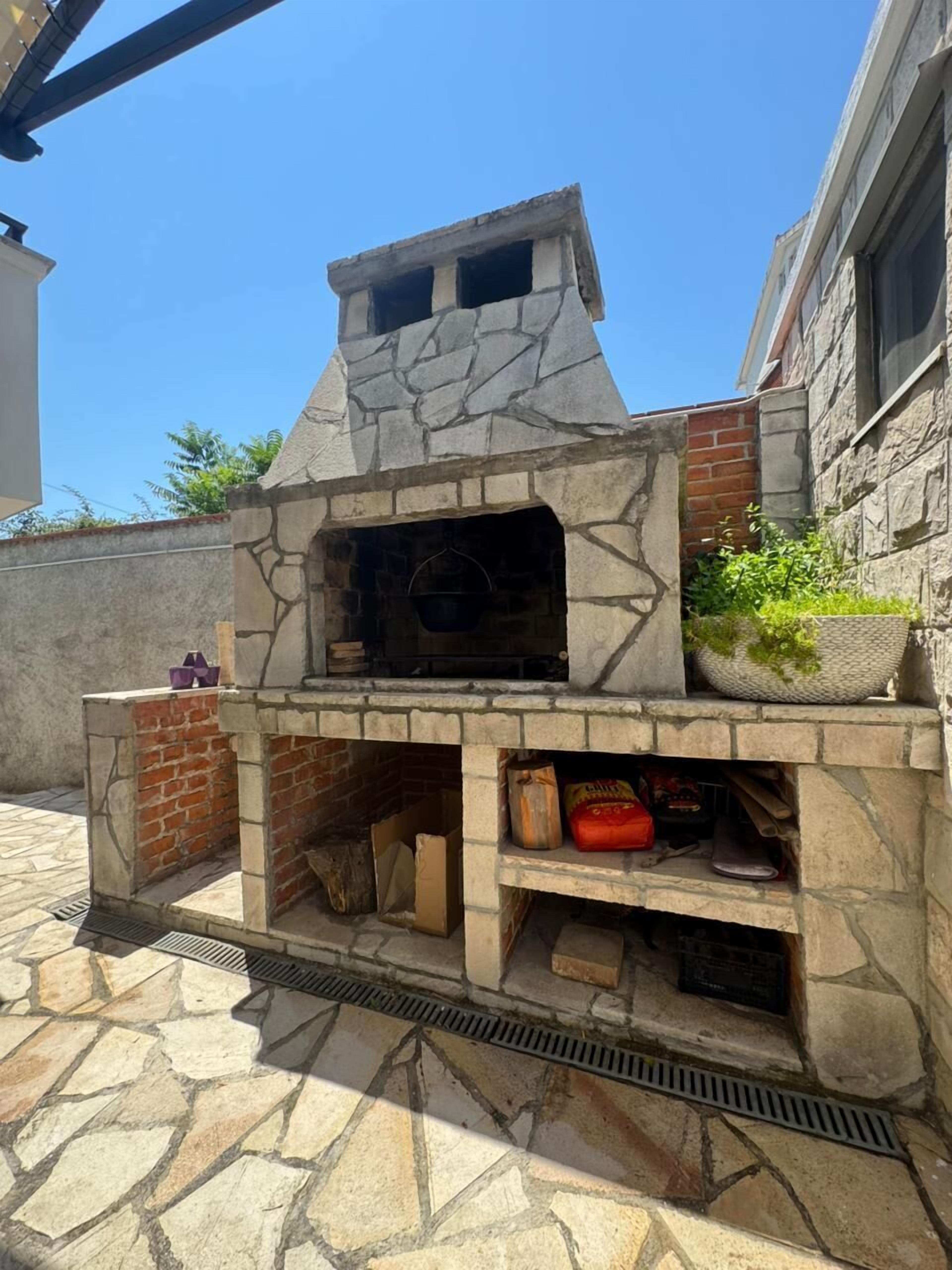 A stone-built outdoor oven with a brick base, a stone chimney, and a planter with greenery on top.