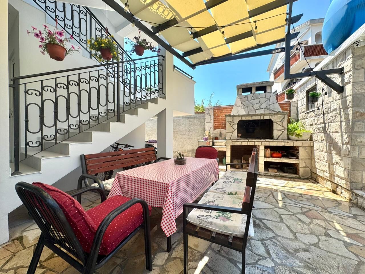 An outdoor patio with a table and chairs, a stone floor, a staircase, and a brick oven.