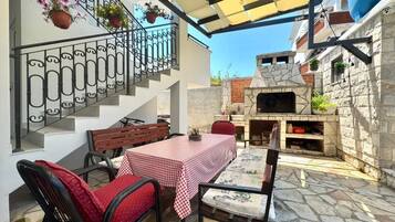 An outdoor patio with a table and chairs, a stone floor, a staircase, and a brick oven.
